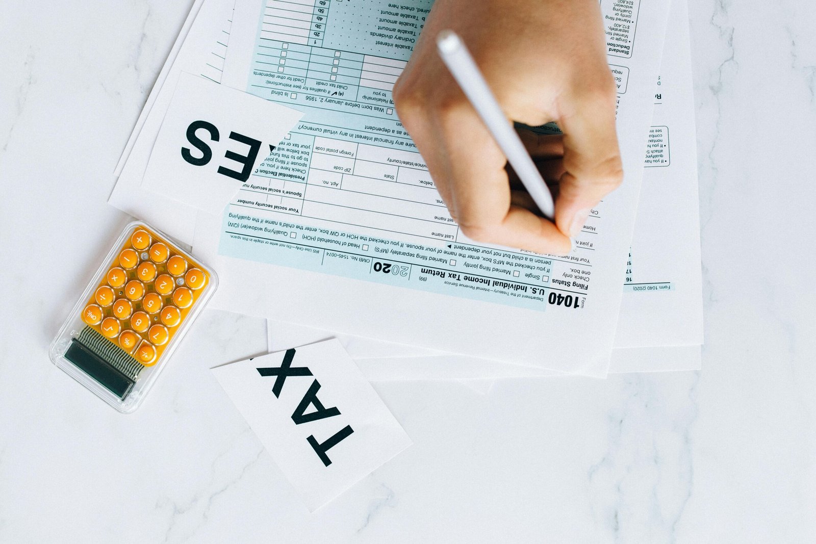 Close-up of hand writing on tax form with calculator nearby on white surface.